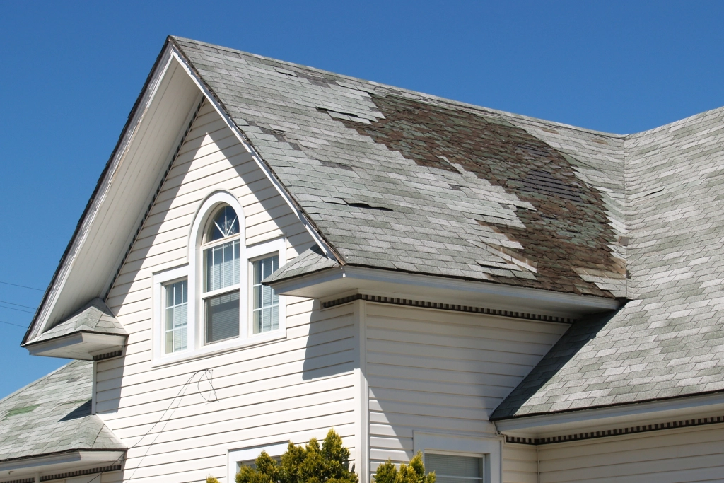 White house with storm damaged shingles and a leaky roof