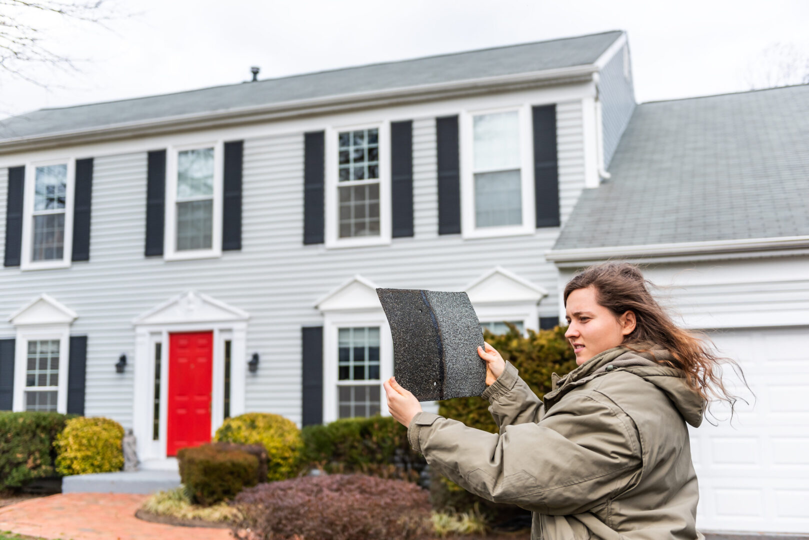 Woman holding a shingle missing from her roof, a sure sign of roof wind damage.